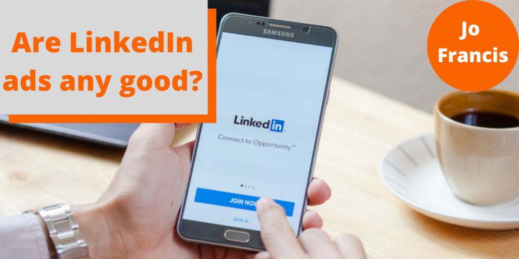 An image of a hand holding a phone one the sign up page for LinkedIn. Also on the table is a laptop and a cup of coffee. On the left side of the image there is an orange rectangle with a grey rectangle layered over the top with orange text reading ‘Are LinkedIn ads any good?’ and on the right side of the image there is an orange circle with white text reading ‘Jo Francis’