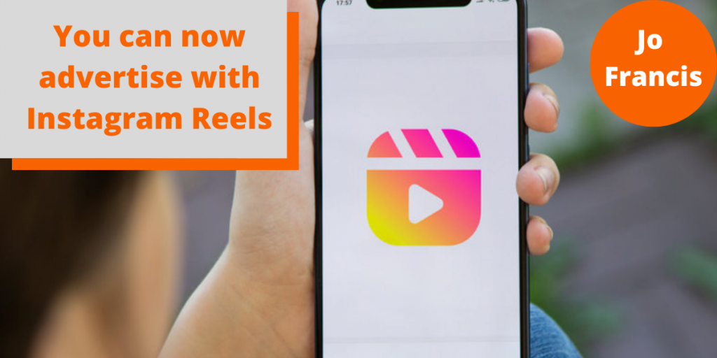An image of a hand holding a phone showing the instagram Reels logo. On the left side of the image there is an orange rectangle with a grey rectangle layered over the top with orange text reading ‘You can now advertise with Instagram Reels’ and on the right side of the image there is an orange circle with white text reading ‘Jo Francis’